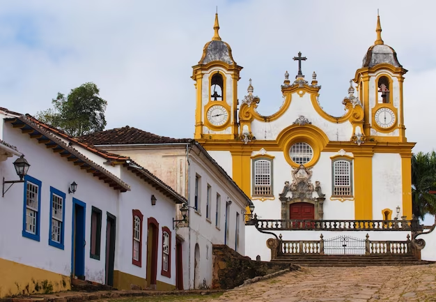 Ah, Tiradentes, uma bela cidade histórica no coração de Minas Gerais! Aqui estão algumas informações úteis para a sua viagem turística a Tiradentes:

Clima: Tiradentes possui um clima tropical de altitude, o que significa que as temperaturas são amenas durante todo o ano. No entanto, é bom estar preparado para mudanças de temperatura, especialmente durante as noites, quando pode esfriar um pouco mais.

Melhor época para visitar: A melhor época para visitar Tiradentes é durante a temporada seca, que vai de abril a setembro. Nesse período, as chuvas são menos frequentes e as temperaturas são mais amenas, tornando a experiência mais agradável.

Atrações turísticas: Tiradentes é rica em história e cultura. Não deixe de visitar o Museu da Liturgia, a Igreja Matriz de Santo Antônio, a Rua Direita com suas lojas e restaurantes charmosos, e o Largo das Forras, onde ocorre a famosa Feira de Artesanato aos finais de semana.

Gastronomia: A cidade é conhecida por sua culinária mineira tradicional. Experimente pratos típicos como o feijão tropeiro, o frango com quiabo e a famosa canjiquinha com costelinha.

Passeios ao redor: Além de Tiradentes, você também pode aproveitar para visitar a cidade vizinha de São João del Rei, que também possui um centro histórico encantador. Não deixe de fazer um passeio de Maria Fumaça, uma locomotiva a vapor que percorre a estrada de ferro entre as duas cidades.

Hospedagem: Tiradentes oferece uma variedade de opções de hospedagem, desde pousadas charmosas até hotéis boutique. Recomendo reservar com antecedência, especialmente durante feriados e festivais, para garantir o melhor lugar para se hospedar.

Lembre-se de sempre respeitar a cultura local, seguir as orientações dos moradores e desfrutar da beleza e tranquilidade desta encantadora cidade histórica. Aproveite a sua viagem a Tiradentes!